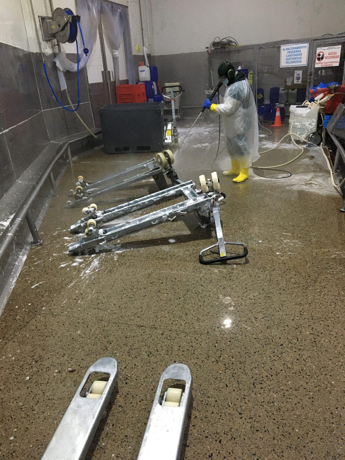Operario aplicando agua a presión sobre equipo industrial durante un procedimiento de higiene sanitaria.
